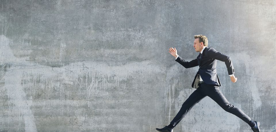 72543591 - side view of man in suit caught in jump making pose of walking on grey wall